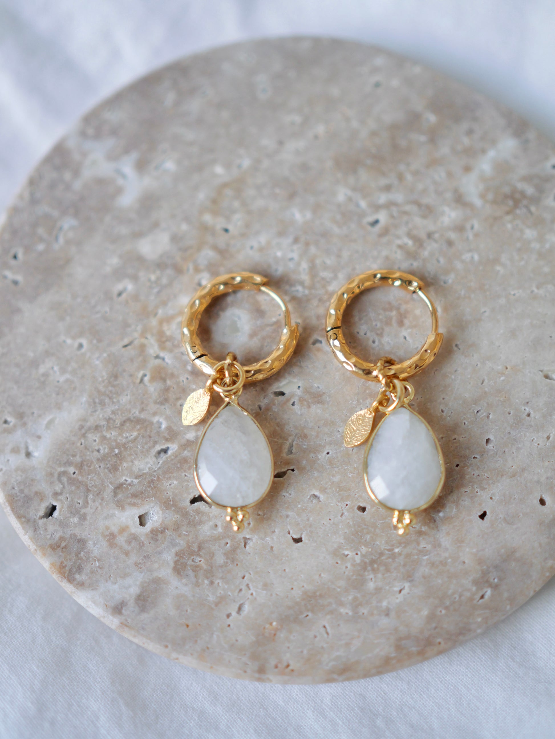 Gold hoop earrings with teardrop-shaped white stones on a stone surface